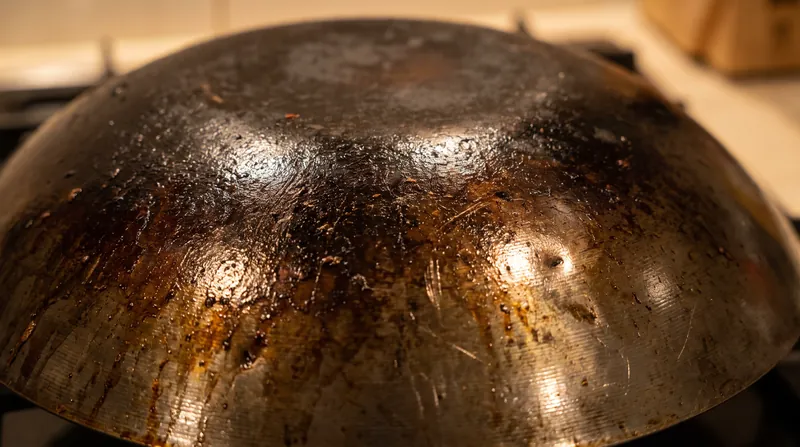 The microscopic patina of polymerized oil on a carbon-steel wok prevents sticking during the high-speed translation phase.