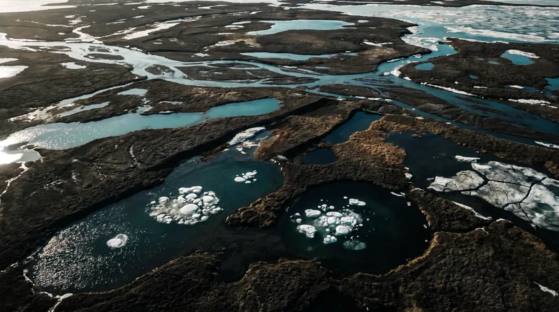 Aerial view of thawing permafrost and meltwater pools in the Arctic landscape.