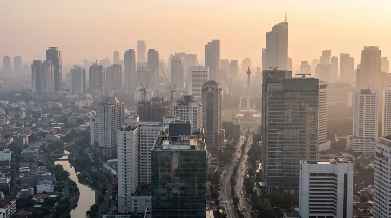 A wide view of the Jakarta skyline at dawn, showing dense high-rise buildings under a calm morning sky.