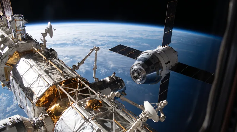 A spacecraft slowly approaching a large modular space station in low Earth orbit against the backdrop of the Earth.