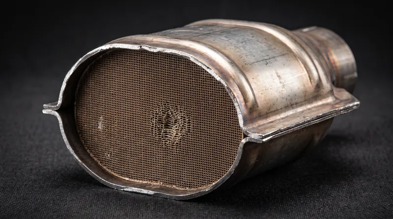A cutaway view of a metallic catalytic converter revealing the dense ceramic honeycomb structure inside.