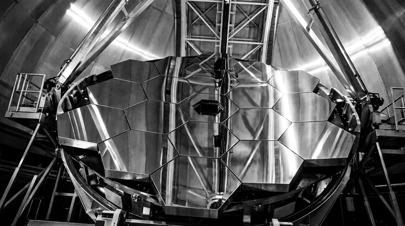 A massive, curved primary mirror of a professional observatory telescope reflecting the surrounding structure.