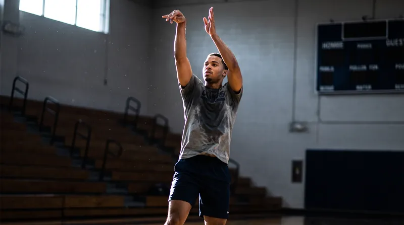 A basketball player in athletic gear follows through on a jump shot in a practice gym.