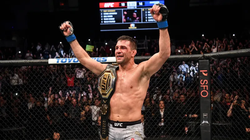 A victorious mixed martial arts fighter stands in the center of the octagon with arms raised.