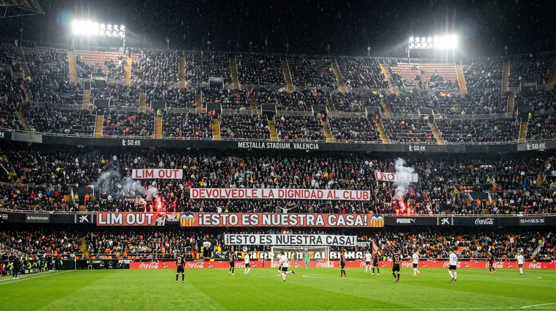 Wide view of the Mestalla stadium in Valencia, Spain, illuminated during a tense evening soccer match.