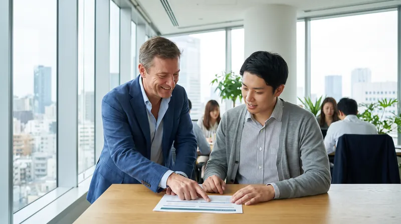 A corporate manager and an employee sitting at a desk in a modern office, reviewing a document together.