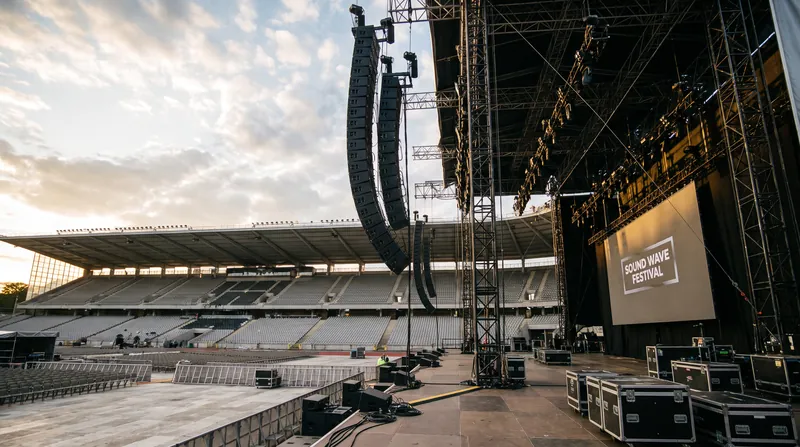 Towering black curved columns of line array speakers hanging from stage rigging at an outdoor stadium concert.