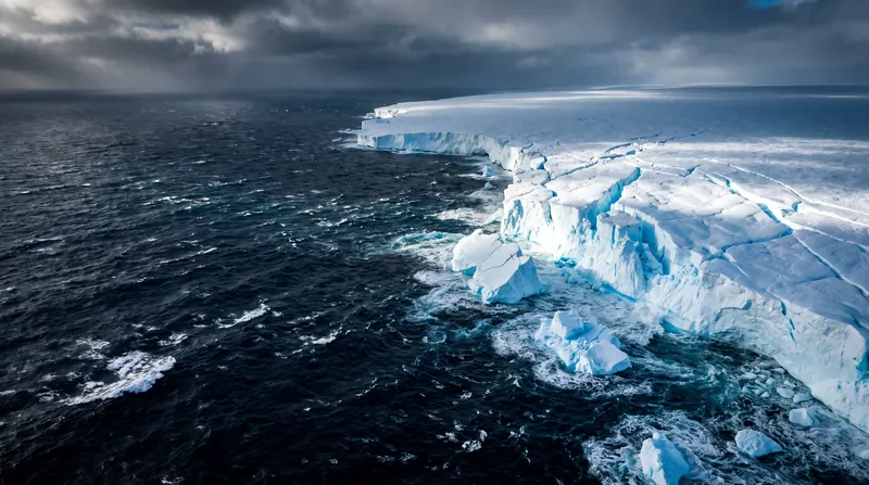 Aerial view of dark blue ocean water meeting the edge of a massive white glacial ice shelf.