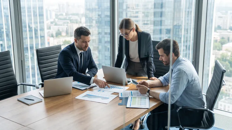 Three corporate professionals reviewing financial documents and compensation data in a modern glass-walled boardroom.