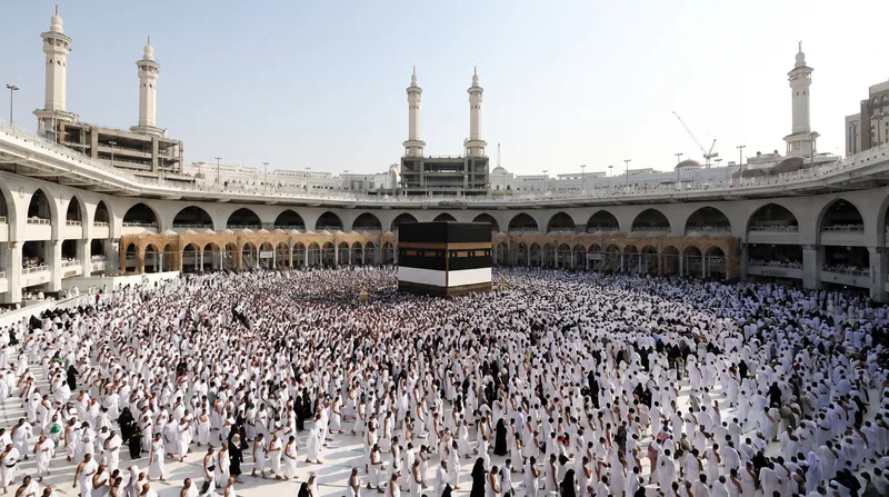 A large crowd of Muslim pilgrims in white robes circumambulating the Kaaba inside the Grand Mosque in Mecca.