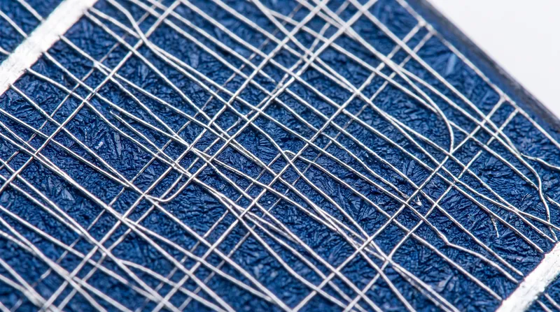 Close-up view of a blue silicon solar cell showing the silver metal grid lines on its surface.