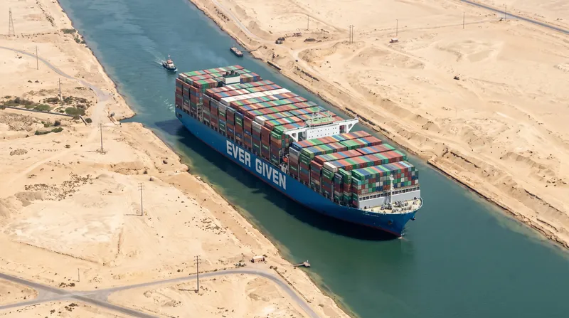Aerial view of a large cargo ship moving through the narrow waterway of the Suez Canal.