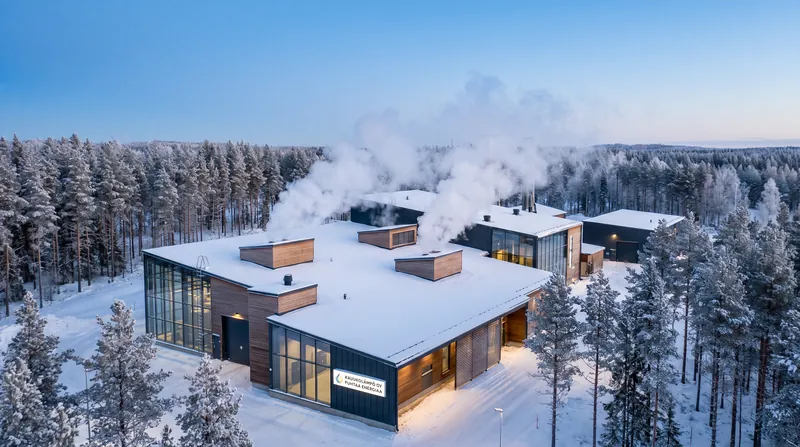 A modern industrial district heating facility in a snowy Nordic environment with steam rising from vents.