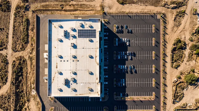 Aerial view of a commercial property showing the building, asphalt parking lot, and surrounding raw land.