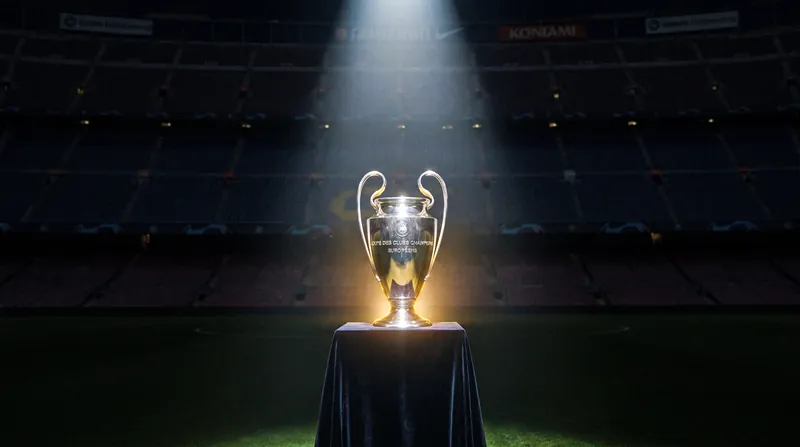The UEFA Champions League trophy displayed on a dark podium under bright stadium spotlights.