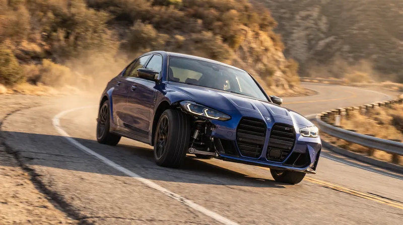A sports sedan cornering aggressively on a winding road, showing visible suspension compression on the outside tires.