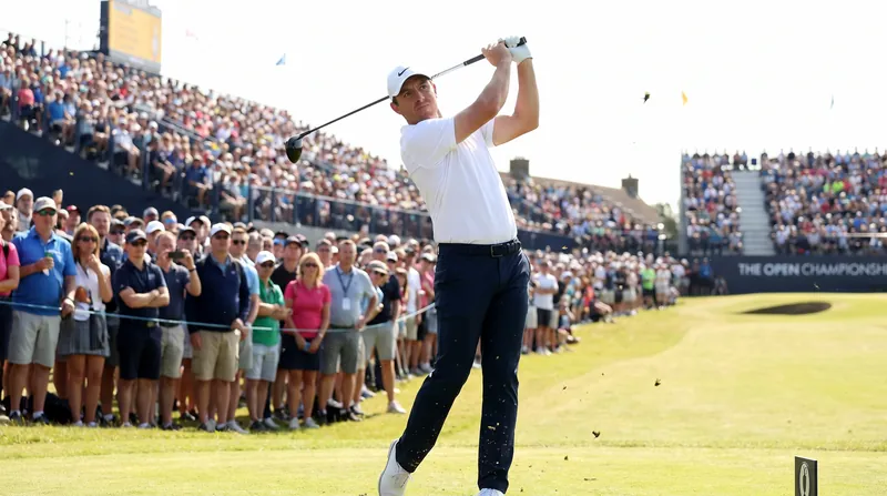 A professional golfer swings a driver off the tee box during a bright, sunny tournament round.