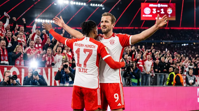 Bayern Munich forwards Michael Olise and Harry Kane celebrating together on the pitch in red kits.