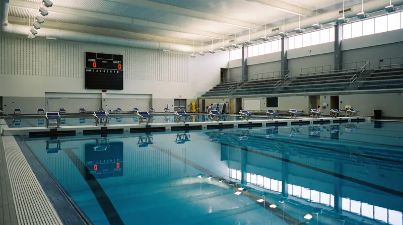 An empty indoor competition swimming pool with starting blocks and calm blue water.