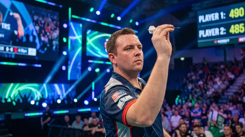 A professional darts player in mid-throw on a brightly lit tournament stage.
