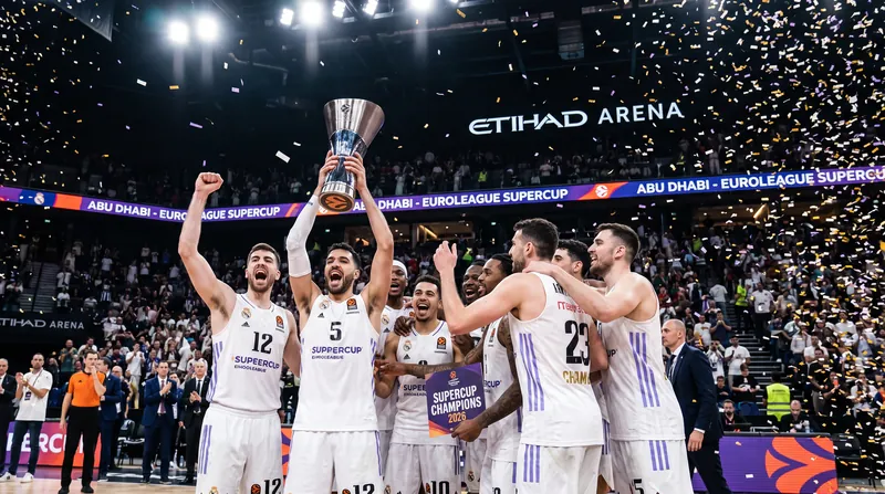 Real Madrid basketball players celebrating on the court with the EuroLeague SuperCup trophy amid falling confetti.
