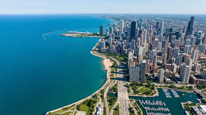 Aerial view of a large blue freshwater lake meeting a dense city shoreline under bright daylight.