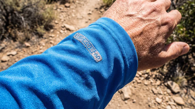 A close-up view of a bright blue synthetic hiking shirt stretched over a hand under bright sunlight.