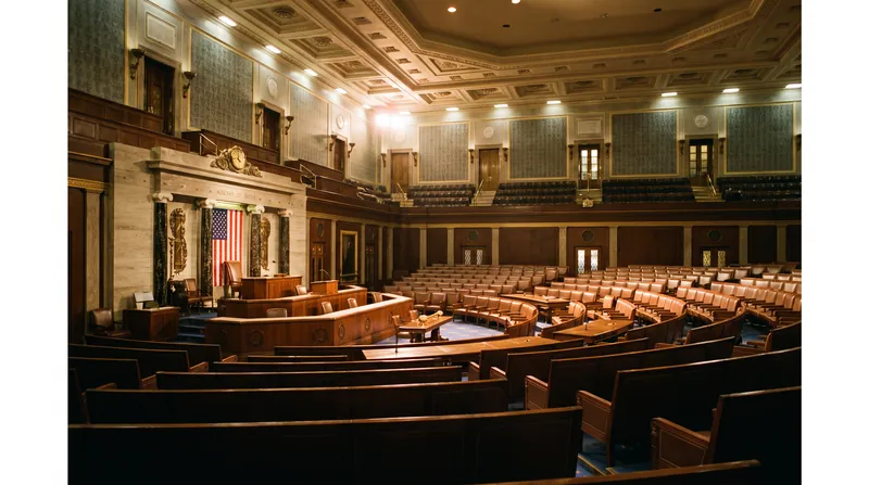 A wide view of the United States House of Representatives chamber showing rows of empty seats and the central rostrum.