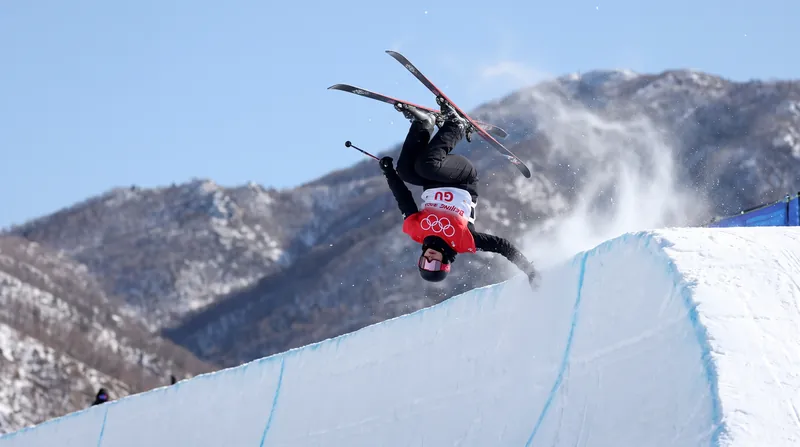 Freeskier Eileen Gu in mid-air executing a trick over a snow-covered superpipe.