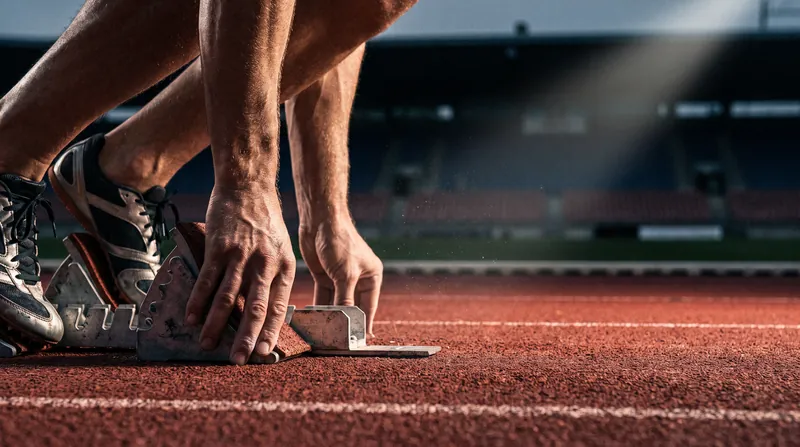 A close-up view of a sprinter's hands and feet positioned in starting blocks on a red running track.