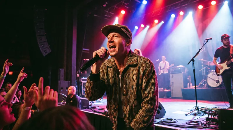 Rapper Macklemore performing on stage holding a microphone under bright concert lighting.