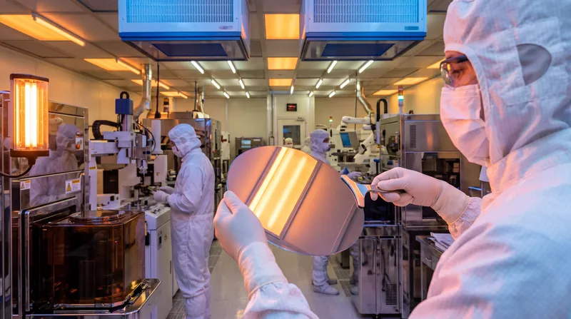 A pristine silicon wafer being handled in a cleanroom under amber lighting.
