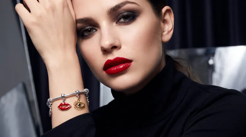 A model wearing bold makeup and a silver charm bracelet with lip and eye charms from the Pandora x Pat McGrath collection.