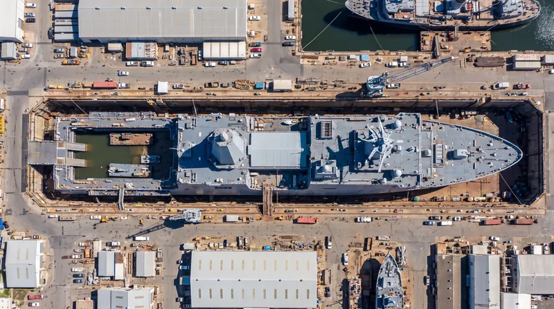 Overhead satellite view of a massive 204-meter gray naval mothership under construction in a drydock, featuring a large enclosed superstructure.