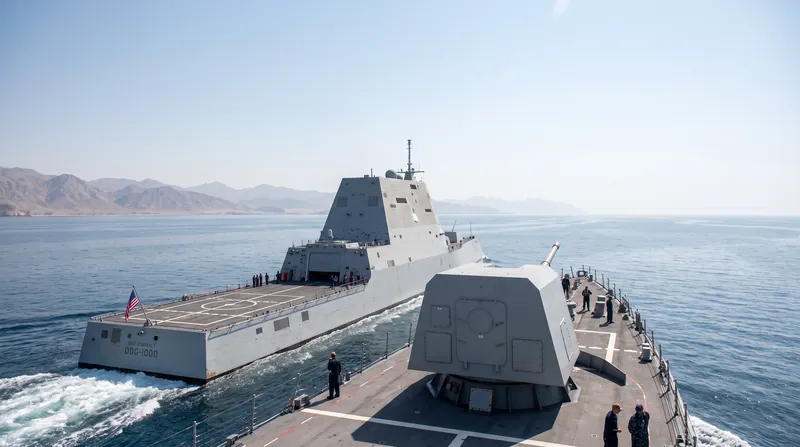 A U.S. Navy warship equipped with a futuristic directed-energy laser weapon turret navigating the Strait of Hormuz.