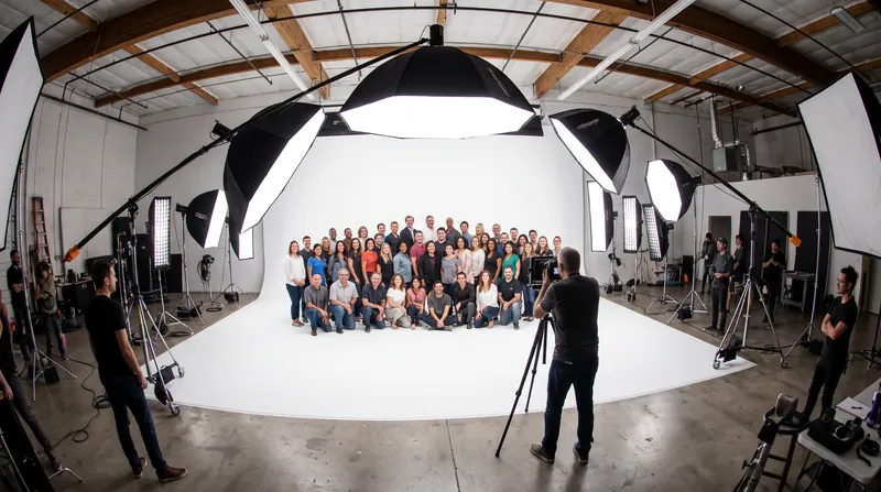 Placing the light source further away utilizes the flat tail of the falloff curve, ensuring even exposure for large groups.