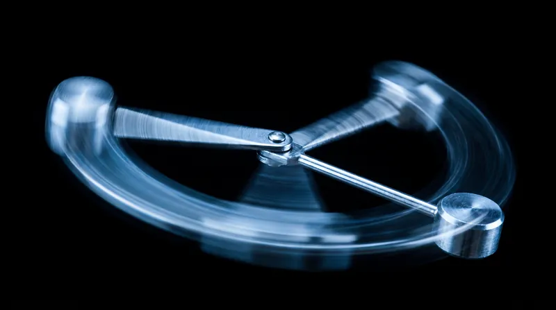 A metallic double pendulum swinging against a dark background, captured with motion blur to show chaotic movement.