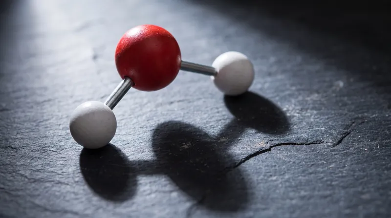 A physical ball-and-stick model of a water molecule resting on a dark laboratory bench.
