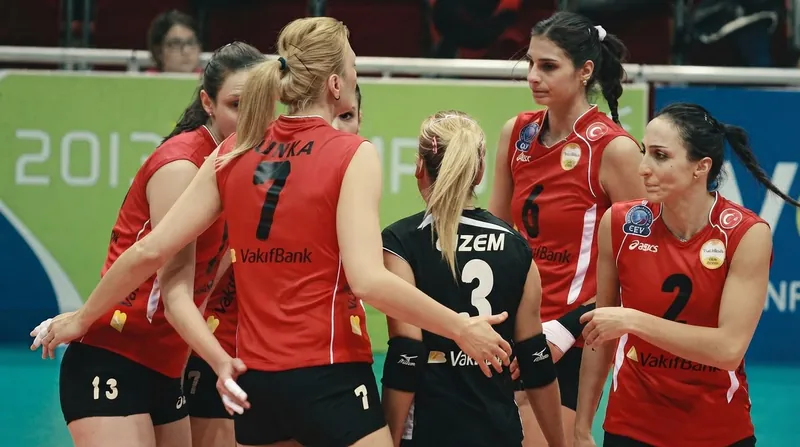 Women's volleyball players in yellow and black uniforms celebrating a point on the court.