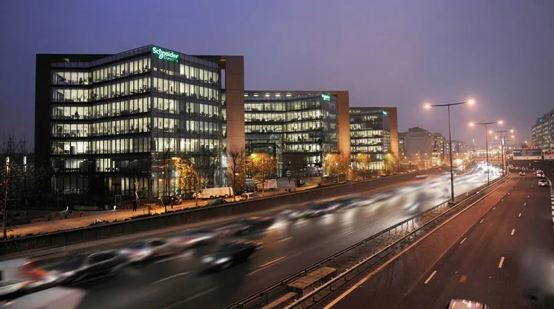 A modern glass-and-steel corporate building belonging to Schneider Electric, featuring green branding on a bright day.