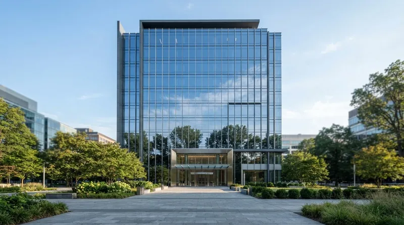 A modern commercial office building exterior at dusk with warm interior lights viewed from street level.