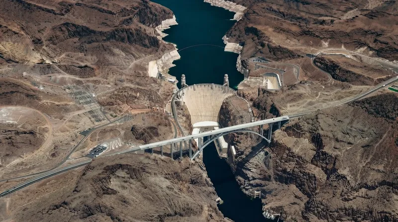 A concrete dam spillway releasing a powerful torrent of clear water into a rocky, eroded riverbed.