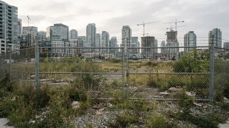 A cracked asphalt surface parking lot sits completely empty in the middle of a dense downtown metropolis surrounded by glass skyscrapers.