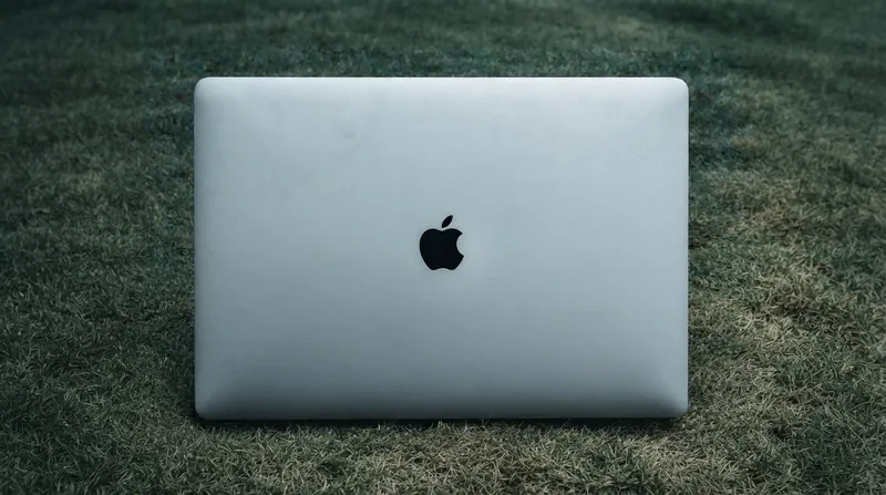 A modern silver laptop slightly open on a desk with a hand touching the screen.
