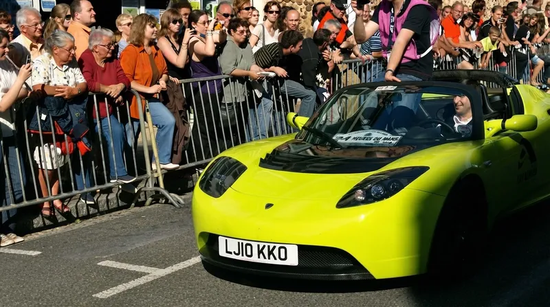 A sleek red Tesla Roadster prototype displayed on a brightly lit presentation stage.