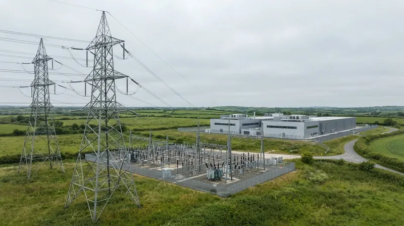 A large electrical substation with heavy transmission lines next to an unfinished commercial construction site.
