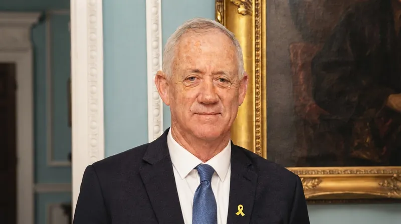 Benny Gantz standing at a podium delivering a speech in a dark suit.