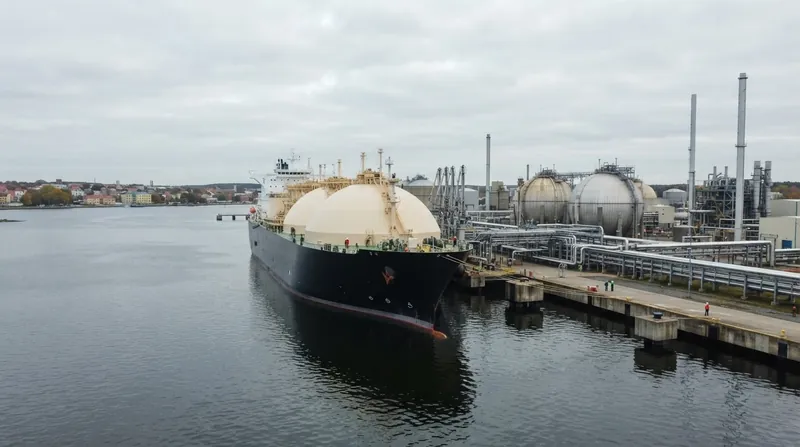 A massive liquefied natural gas carrier ship docked at an industrial European import terminal at dusk.