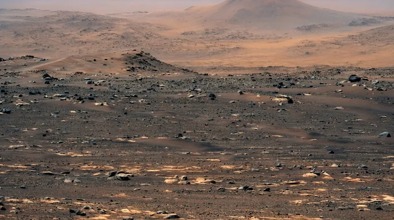 The six-wheeled Perseverance rover drives across a rocky, rust-colored Martian landscape under bright sunlight.