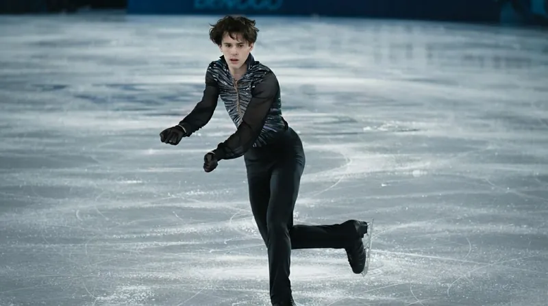 A male figure skater in mid-air during a jump in a brightly lit competition arena.